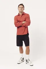 Buzo de algodón tipo polo con cuello camisero, cierre frontal con botones y mangas largas. Presenta un diseño liso en color terracota con logo bordado sutil en el pecho.
