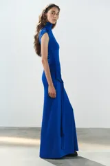 Vestido largo color azul, confeccionado en tejido elástico, con cuello alto, manga muy corta y detalle de lazada en la cintura. Cuenta con abertura en la espalda.