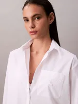 Camisa de corte relaxed confeccionada en popelina de algodón con elastano. Presenta cuello de punta clásico, cierre frontal con botones, mangas largas y un bolsillo en el pecho con el monograma CK bordado en relieve.