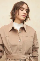 Sobrecamisa de pana color beige, con cuello camisero, cierre frontal con botones metálicos, mangas largas con puños abotonados y lazo ajustable en la cintura.