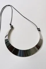 Collar tipo gargantilla de metal plateado pulido con forma de media luna ancha. Se ajusta con un cordón negro anudado.