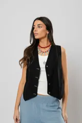 Chaleco negro con escote en V, sin mangas y cierre frontal con botones. Presenta pespuntes en color crudo en la parte delantera y logo bordado en la espalda.