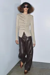 Chaqueta de punto color beige claro, manga larga y cuello redondo. Presenta un detalle de frunces verticales ajustados por botones a tono en el centro frontal.