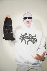Hoodie blanco con pasamontañas negro incorporado, corte oversize, estampado en el pecho y mangas, y bolsillo tipo canguro.