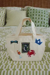 Bolso tote de lienzo crudo, tamaño pequeño, con asas de mano y parches bordados decorativos alusivos al verano.