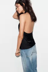 Top de satén con cuello halter, diseño drapeado en el frente y bajo asimétrico. Presenta espalda descubierta y cierre con lazada en el cuello.