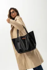 Cartera de cuero color negro, tipo tote bag, con asas finas y un detalle de etiqueta marrón con el logo de la marca en el frente. Incluye doble bolsillo y colgante interno para llaves.