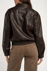 Campera bomber de cuero sintético marrón, con cierre frontal, cuello camisero, bolsillos laterales y elástico en los puños y la cintura.