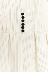 Blazer entallado de color crema con rayas verticales finas, cuello sin solapa y manga larga con hombreras. Presenta un diseño con bajo en evasé tipo peplum y cierre frontal con botones negros.