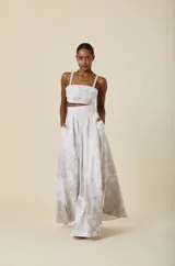Falda larga de corte balloon con volumen, confeccionada en tela con estampado floral en tonos gris y blanco. Presenta una silueta estructurada con pinzas en la cintura y bolsillos laterales.