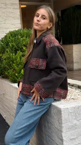 Campera de corte oversize confeccionada en lana merino, con diseño bicolor que combina paneles de color gris oscuro liso con detalles en tejido de punto con textura y estampado a cuadros en tonos rojizos y marrones. Presenta cierre frontal, cuello camisero, bolsillos frontales con solapa y puños con el mismo tejido estampado.