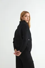 Abrigo de punto negro con cuello alto y cierre frontal completo. Presenta un diseño de corte recto con bolsillos frontales y terminaciones en tejido acanalado.