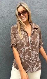 Camisa de corte recto y manga corta con cuello clásico y cierre frontal de botones. Presenta un estampado floral en color blanco sobre una base de color chocolate.