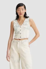 Chaleco crop top de denim color blanco con batik celeste, con cuello en V, cierre frontal con botones y bolsillos con solapa en el pecho.