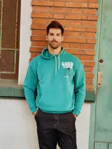 Canguro de algodón peletizado en color verde, con capucha y cordones ajustables. Presenta un bolsillo frontal tipo canguro y un estampado gráfico en el pecho con la frase 'Good Vibes' y un personaje animado.