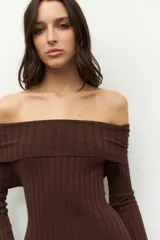 Vestido largo de punto acanalado en color negro, con diseño de hombros descubiertos y mangas largas. Presenta un corte ajustado al cuerpo y aberturas laterales en el ruedo.