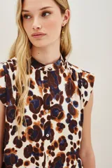 Camisa sin mangas con cuello camisero y botones frontales, confeccionada en tela estampada con patrón animal print en tonos blanco, marrón y azul oscuro.