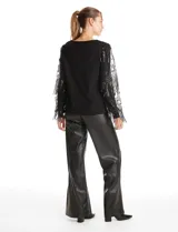Buzo de tejido negro con mangas largas de microtul transparente, decoradas con bordados de lentejuelas y flecos brillantes. Presenta un diseño elegante con cuello redondo.
