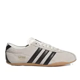 Championes Adidas modelo Tokyo, de diseño retro y perfil bajo. Confeccionados en gamuza color beige con las icónicas tres tiras laterales en cuero negro, forro interno de cuero y suela de caucho color caramelo.