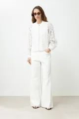 Campera blanca de broderie con cierre frontal, cuello redondo y mangas largas.