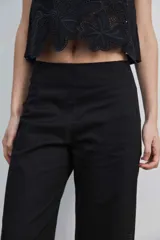 Pantalón negro de tiro alto y corte recto, confeccionado con detalles de bordados florales calados en la parte inferior de las piernas.