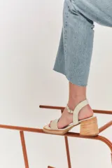 Sandalias de taco cuadrado medio, con base y talón en gamuza color tostado. Presenta una tira frontal de múltiples bandas doradas y una pulsera al tobillo con hebilla metálica.