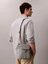 Cartera reporter Calvin Klein color gris, de diseño compacto con solapa frontal y correa ajustable para el hombro. Cuenta con detalles de marca grabados y correa central ajustable.