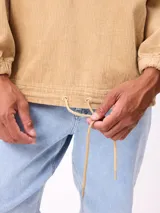 Canguro de pana color tostado con capucha, cordones ajustables, cierre frontal parcial con botones y dos bolsillos delanteros. Presenta puños elásticos y un diseño de calce relajado.