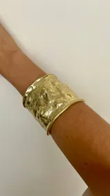 Brazalete ancho dorado con textura irregular.