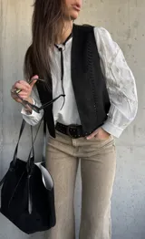 Chaleco negro de gamuza sintética, de estilo boho-chic, con costuras decorativas en los bordes y diseño clásico atemporal.