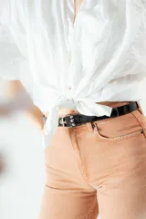 Cinturón negro de cuero charol con hebilla metálica plateada y ojales metálicos.