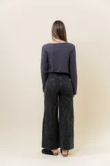 Pantalón de jean negro de pierna ancha y tiro medio-alto, con estampado sutil de leopardo en tono más oscuro y pequeños puntos blancos brillantes.