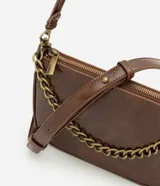 Cartera femenina modelo baguette Satinato confeccionada en PU marrón, de tamaño pequeño y estructura compacta con base levemente curvada. Cuenta con cierre superior, cadena frontal robusta en metal y asa transversal desmontable.