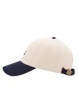 Gorra Archive de color beige con visera y botón superior azul marino. Cuenta con mensaje bordado en el lateral y cierre regulable con hebilla metálica.