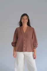 Blusa color chocolate con cuello en V, cierre frontal con botones y mangas largas abullonadas con puños elásticos. Presenta detalles de bordado lineal a lo largo de la abertura frontal.