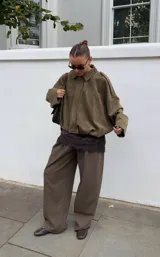 Chaqueta tipo bomber de gamuza en color verde oliva, con cuello camisero, cierre frontal oculto y diseño de corte holgado con hombros caídos.