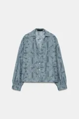 Camisa de manga larga color celeste con cuello solapa, escote en V y cierre frontal con botones. Presenta un diseño con bordados perforados y patrones geométricos y florales.