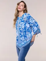 Blusa de gasa azul con estampado floral y geométrico estilo pañuelo, escote redondo, mangas tres cuartos amplias con jareta ajustable y ruedo asimétrico en punta.