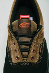 Championes Vans modelo Skate Era Wafflecup, con diseño bicolor en negro y marrón. Presentan una silueta clásica de skate con suela WaffleCup que combina durabilidad y flexibilidad, cordones negros y detalles en color naranja en la lengüeta, plantilla y suela.