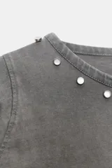 Camiseta de manga larga color gris con efecto lavado, cuello redondo y bajo redondeado. Presenta aplicaciones de tachas metálicas alrededor del escote y en el bajo.