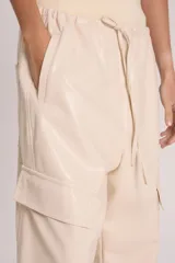 Pantalón babucha color crema de cuero sintético, tipo cargo, con cintura elastizada y lazo de ajuste.