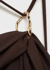 Traje de baño enterizo marrón chocolate con diseño drapeado, cuello asimétrico con tirante fino y aro decorativo dorado.