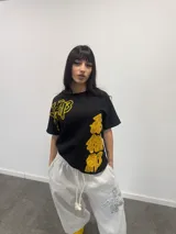 Remera negra de corte regular con estampado gráfico en color amarillo. Presenta inscripciones con estética oriental en la parte superior izquierda y en el lateral derecho. Confeccionada en algodón de alto gramaje con cuello reforzado y grifa de la marca en la manga.
