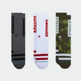 Pack de tres pares de medias deportivas Stance, caña media. Incluye un par gris oscuro con franjas negras, un par blanco con franjas rojas y un par con estampado camuflado verde oliva. Todas las medias llevan el logo de Stance en la caña.