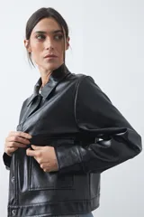 Chaqueta de cuero sintético negro con acabado brillante, cuello camisero, cierre frontal con botones a presión y bolsillos frontales con solapa.