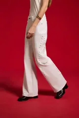 Pantalón jean blanco de corte flare y tiro alto, con detalles de tachas a lo largo de las costuras laterales y botamanga sin costura.