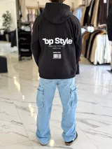 Canguro negro oversize con capucha y gran estampado blanco en la espalda con el texto "Top Style", "Dream big. Work hard. Make it real.", "SINCE 2021" y un código de barras.
