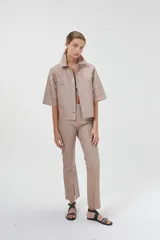 Camisa de cuero ovino color rosa pálido, de corte recto y estilo minimalista. Tiene mangas cortas, cuello clásico, cierre con botones a presión plateados y bolsillos delanteros con solapa.