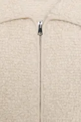 Chaqueta de punto bouclé color crudo, con cuello de solapa grande, manga larga y cierre frontal con cremallera.