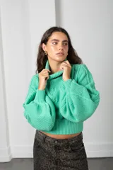 Polera de punto color verde menta, con cuello alto, mangas globo y diseño de trenzas en el frente.